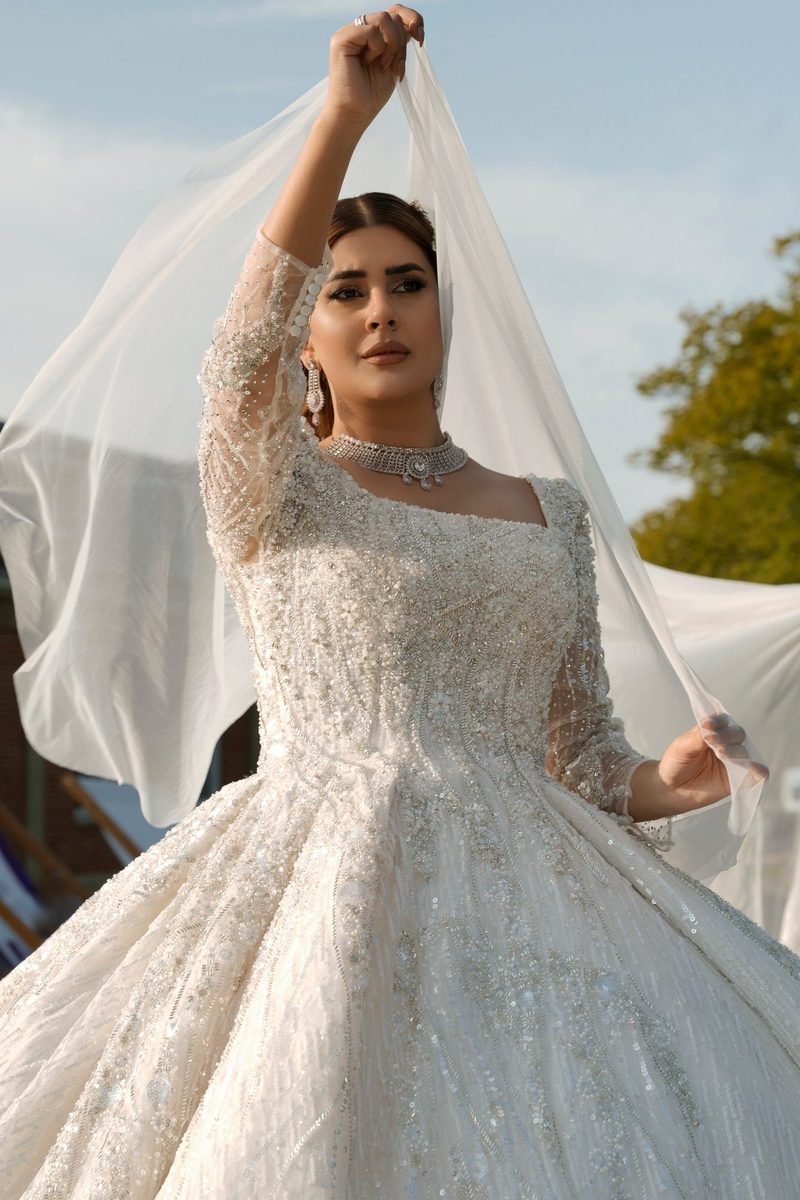Bride in a white beaded ballgown lifting her long veil in soft daylight