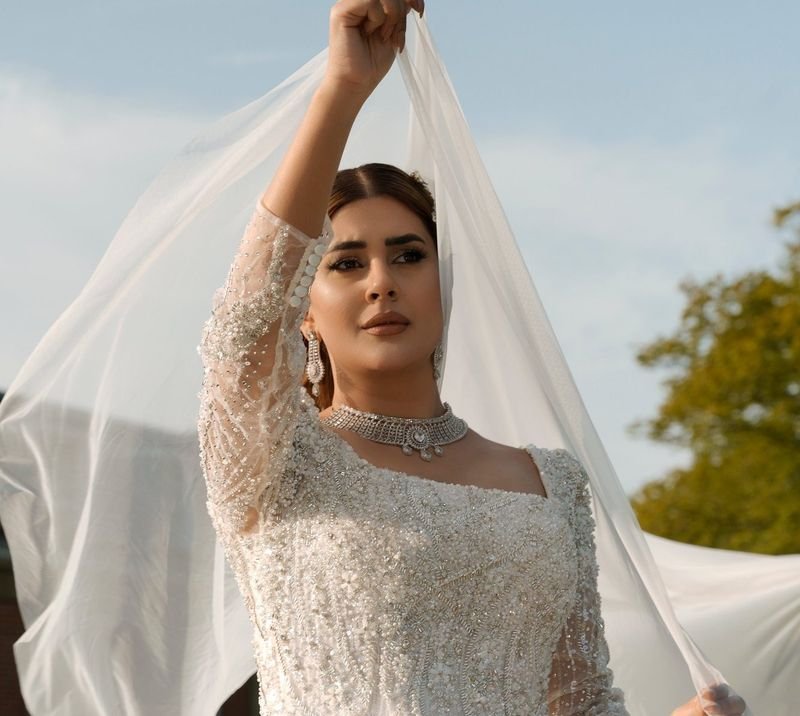 Bride in a white beaded ballgown lifting her long veil in soft daylight
