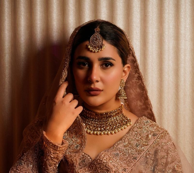 Bride in an embroidered outfit and sheer dupatta wearing a gold choker necklace and maang tikka