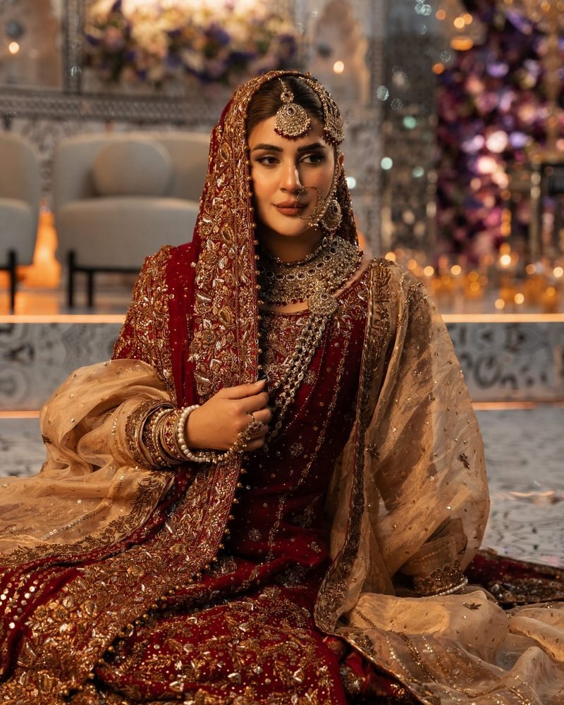 Bride in red and gold with a gold dupatta seated in a candlelit hall with floral decor