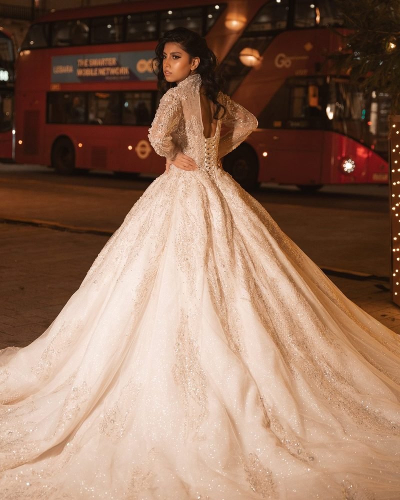 Bride in a lace ball gown with a long train seen from behind, with a red London bus behind her