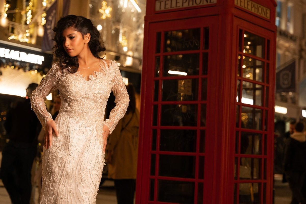 Bride in a lace wedding dress beside a red telephone box on a London street