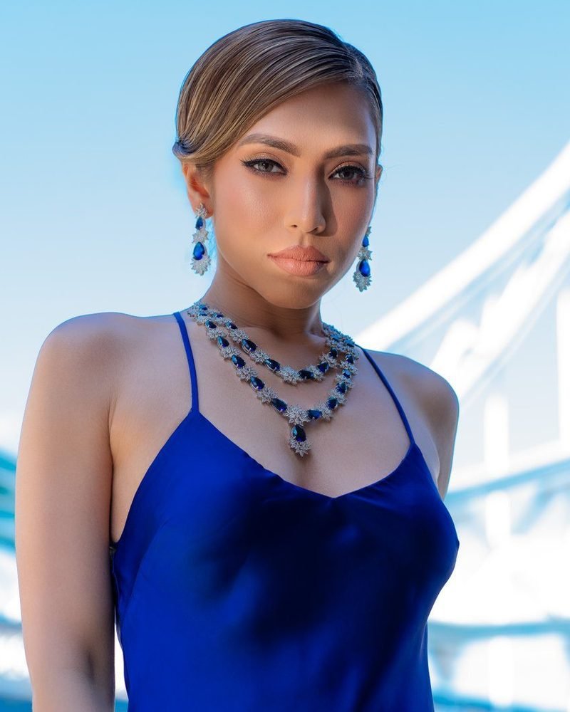 Model in a blue satin top and sapphire necklace with Tower Bridge behind her