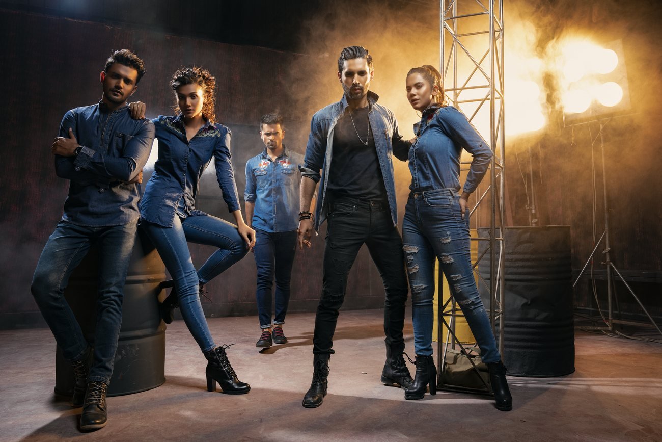Group of models in denim outfits posed around oil drums and studio lights on a smoky industrial set